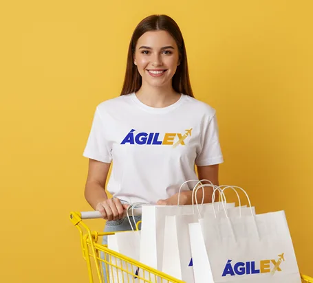 Mujer joven sonriendo con camiseta y bolsas de compras Ágilex sobre fondo amarillo.